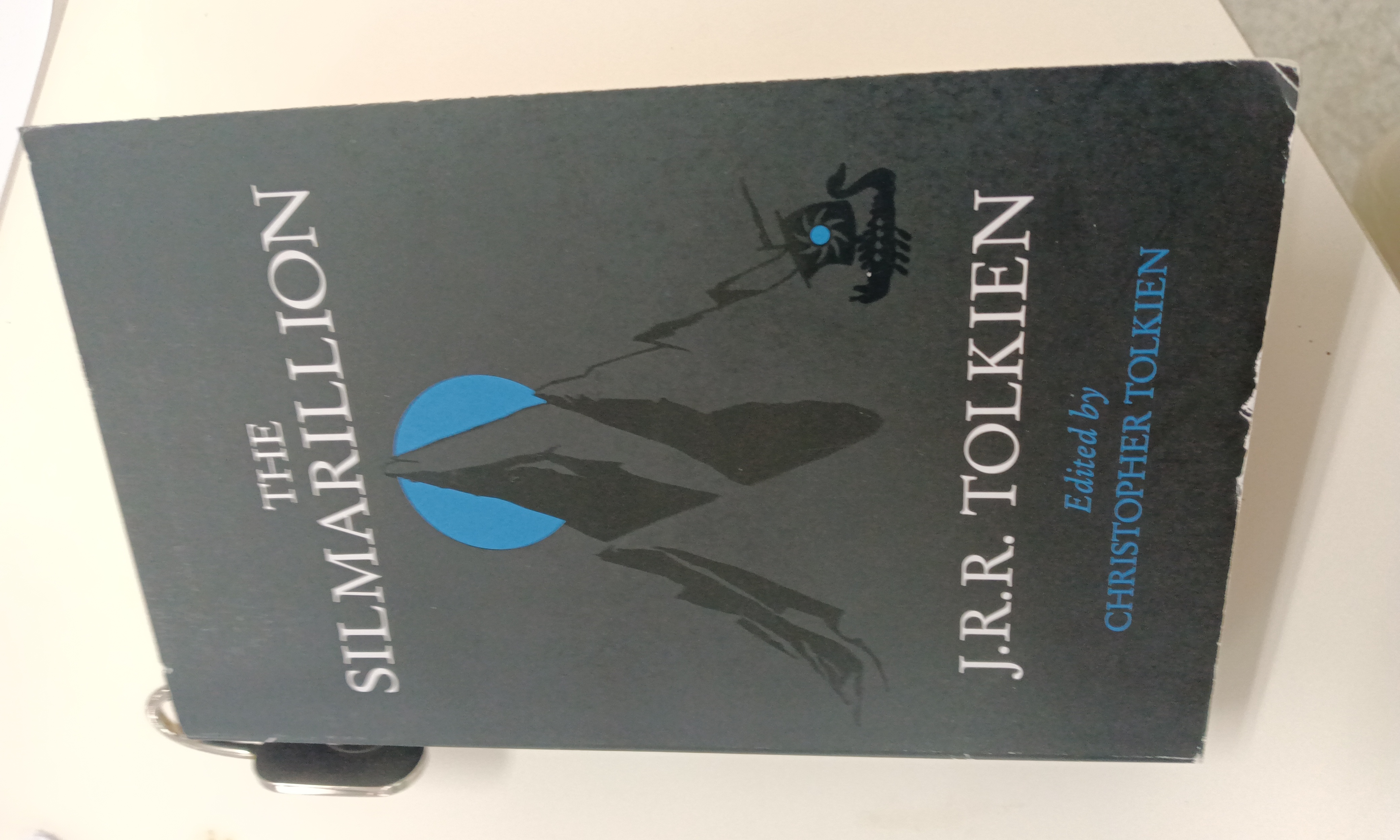 画面中展示了一本封面为深色、带有蓝色圆圈和黑色山脉图案的《精灵宝钻》书籍。 (由 AI 生成标题)