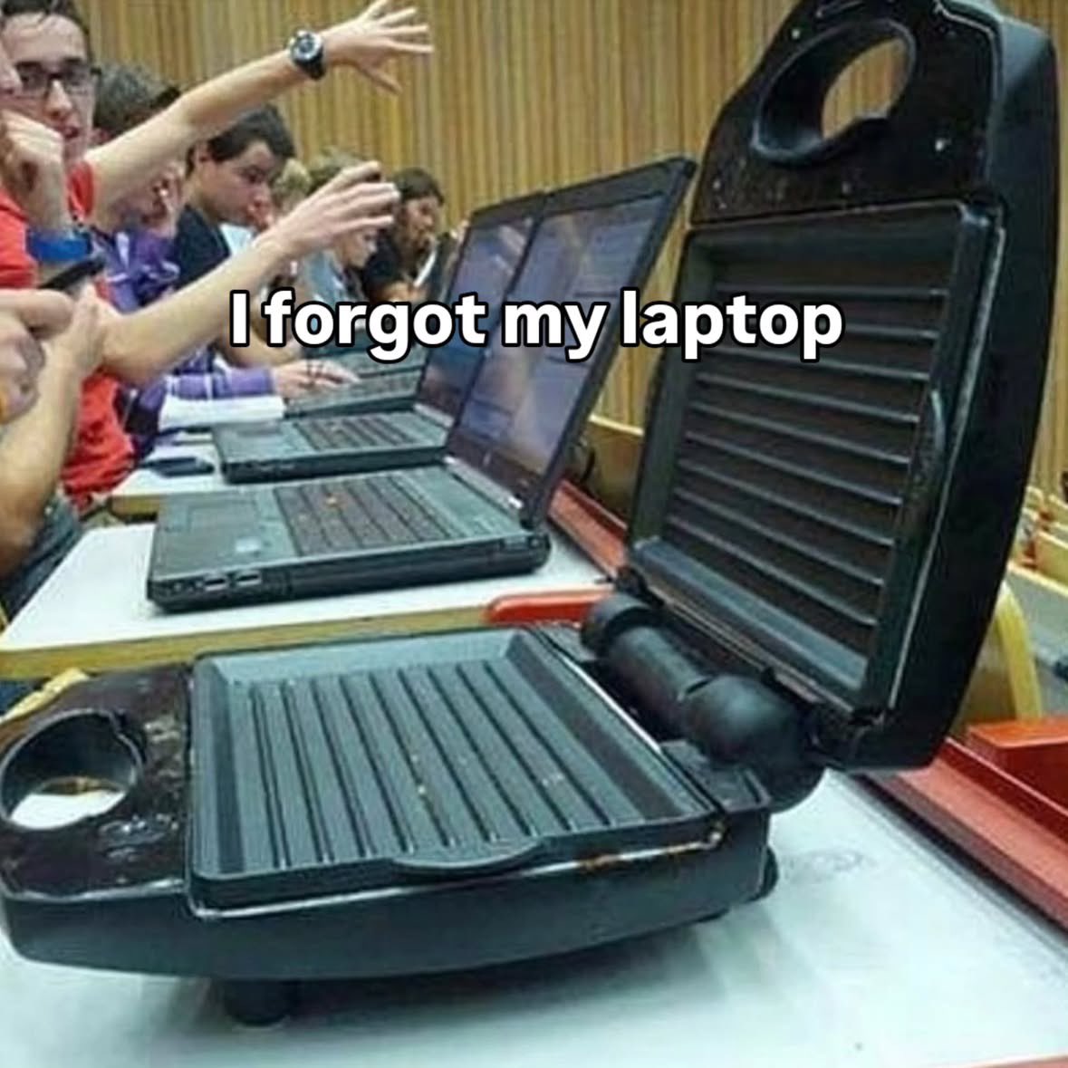 In a classroom setting, an open electric grill sits on a desk among students using actual laptops, humorously captioned "I forgot my laptop". (由 AI 生成标题)